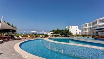 A swimming pool with lounge chairs and umbrellas, surrounded by buildings.