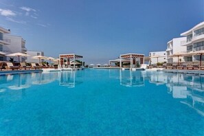 A large swimming pool with sun loungers and umbrellas, surrounded by modern buildings. - VPX Hotel (Asia)
