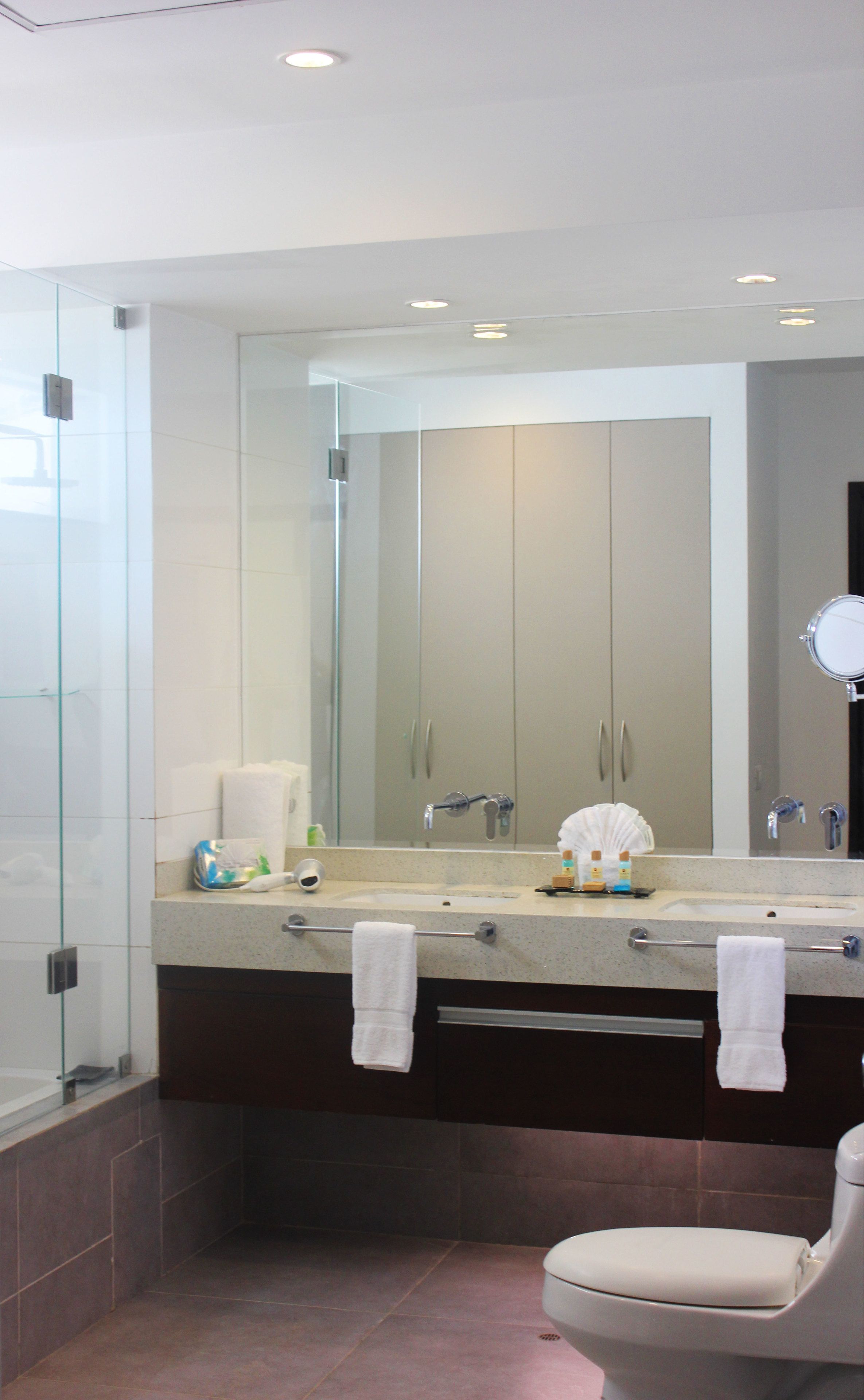 A modern bathroom with a large mirror, a sink with two faucets, a towel rack, and a toilet.