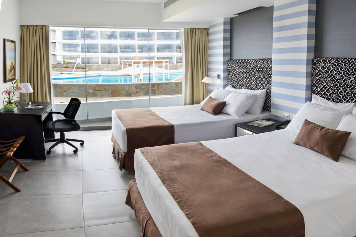 A hotel room with two beds, a desk, and a view of a pool.