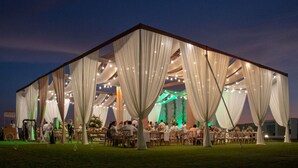 Een grote tent met draperende stof en lichtjes, opgesteld in een grasveld.