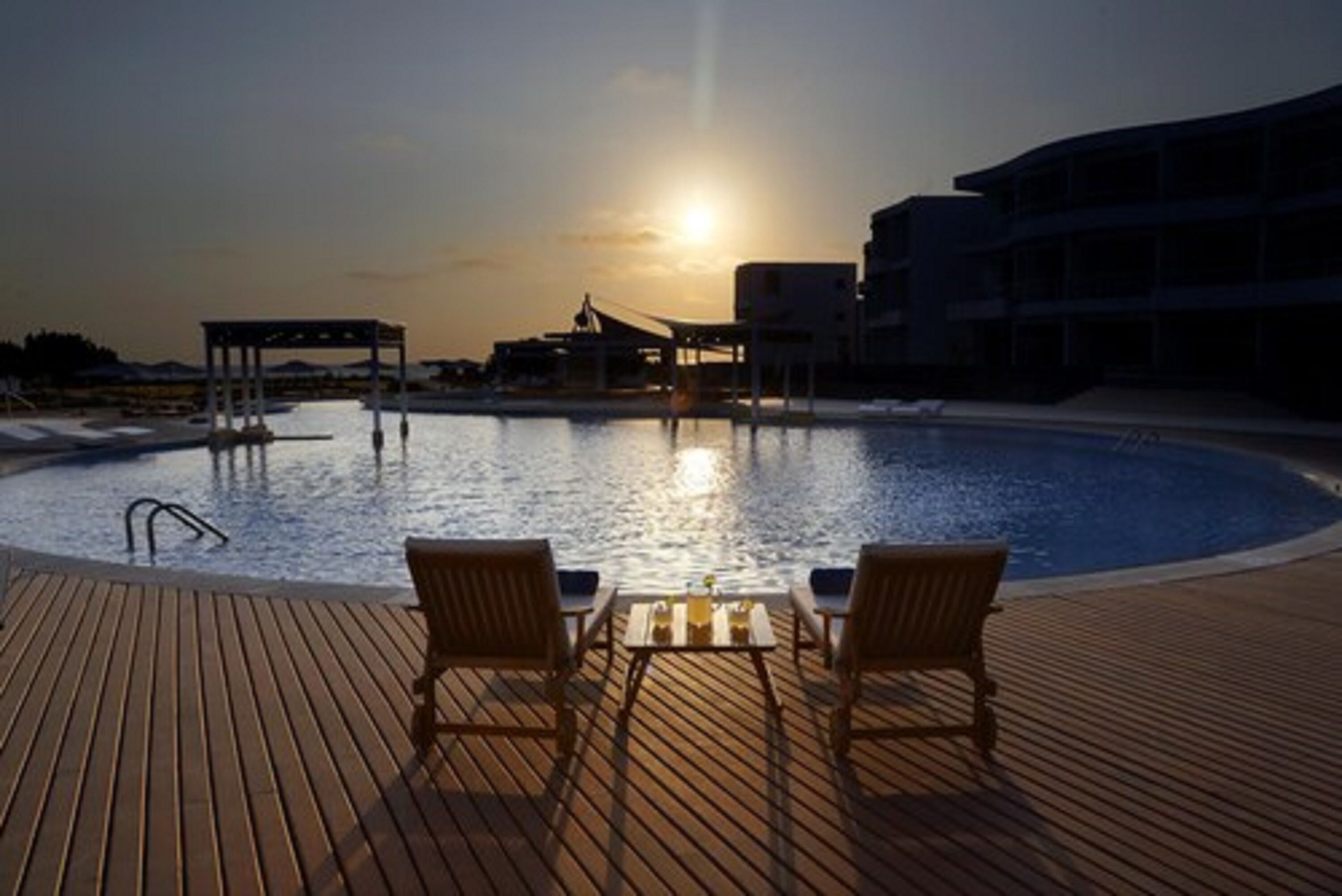 A poolside area with a wooden deck, two lounge chairs, and a table with a drink.