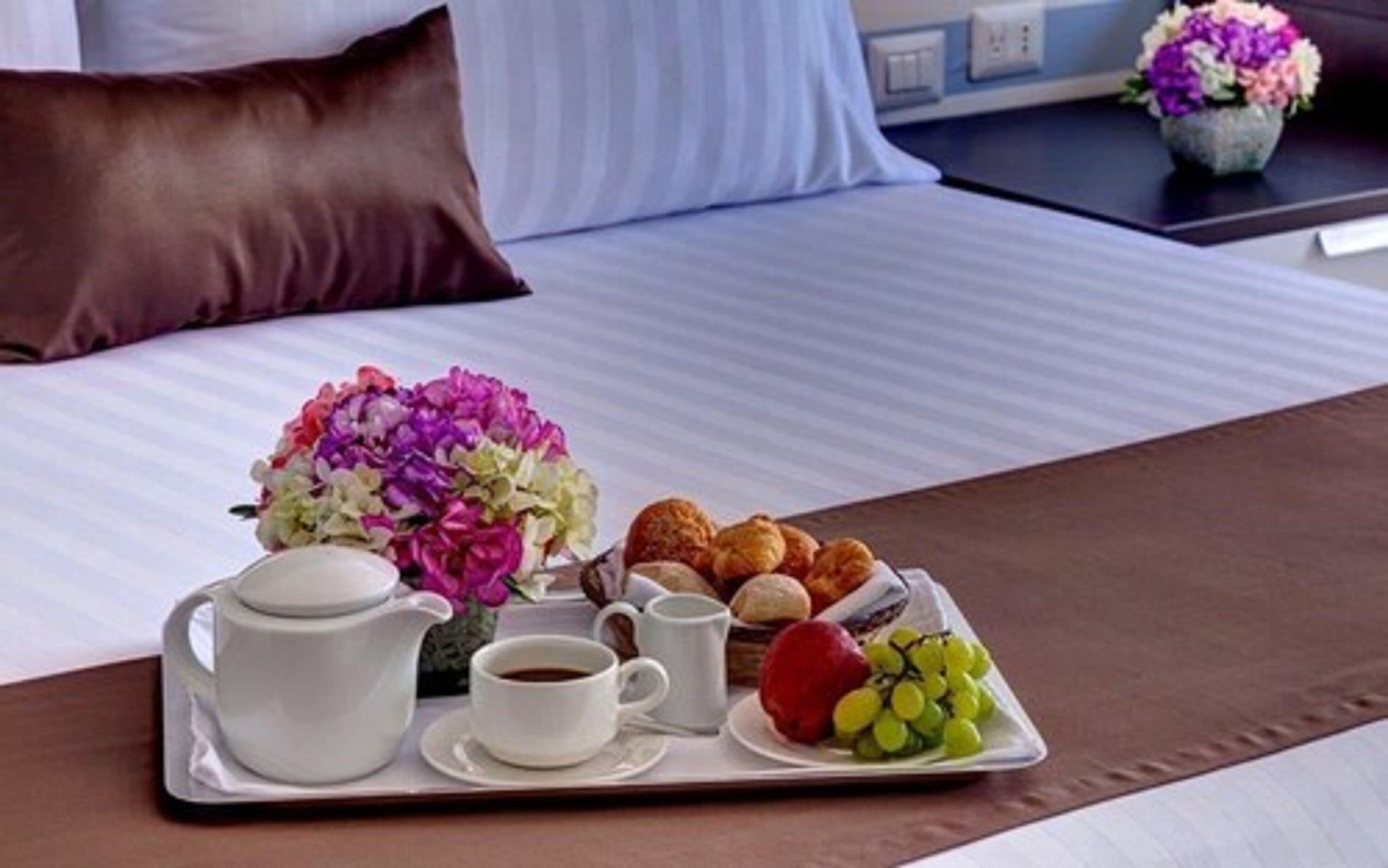 Bandeja de desayuno con té, café, bollería y fruta sobre una cama.