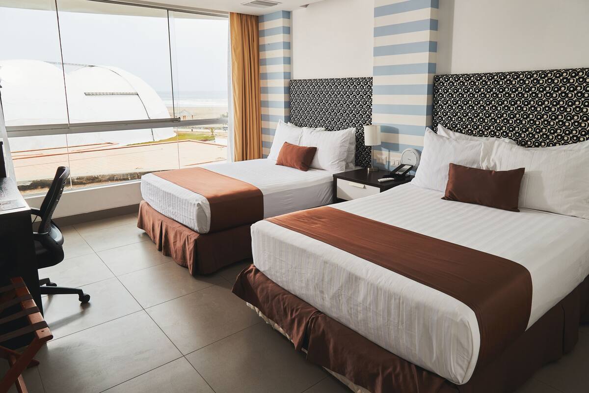 A hotel room with two beds, a desk, and a chair.