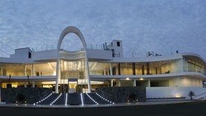 Een modern meerlaags hotel met een opvallende boogentree, meerdere balkons en een goed verlichte gevel.