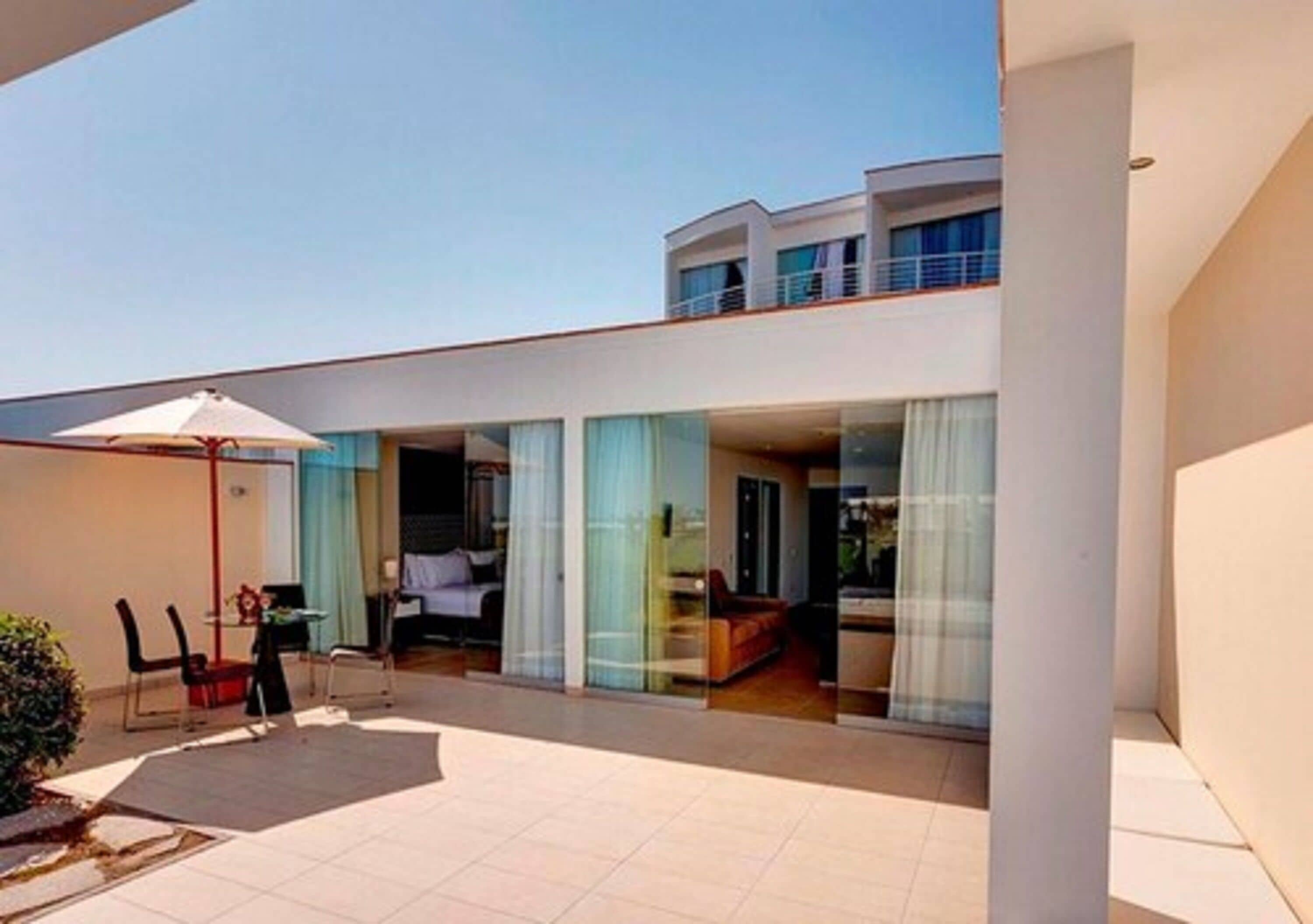 Un hotel moderno con un amplio espacio exterior, que incluye un patio con mesa y sillas, y un balcón con vistas al interior.