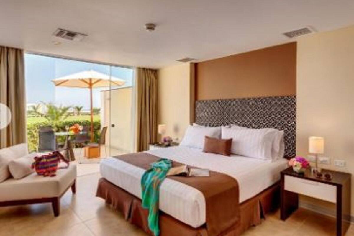 A hotel room with a large bed, a chair, a nightstand, and a view of the outdoors.