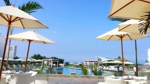 Een zwembadterras met parasols, ligbedden en uitzicht op de oceaan.