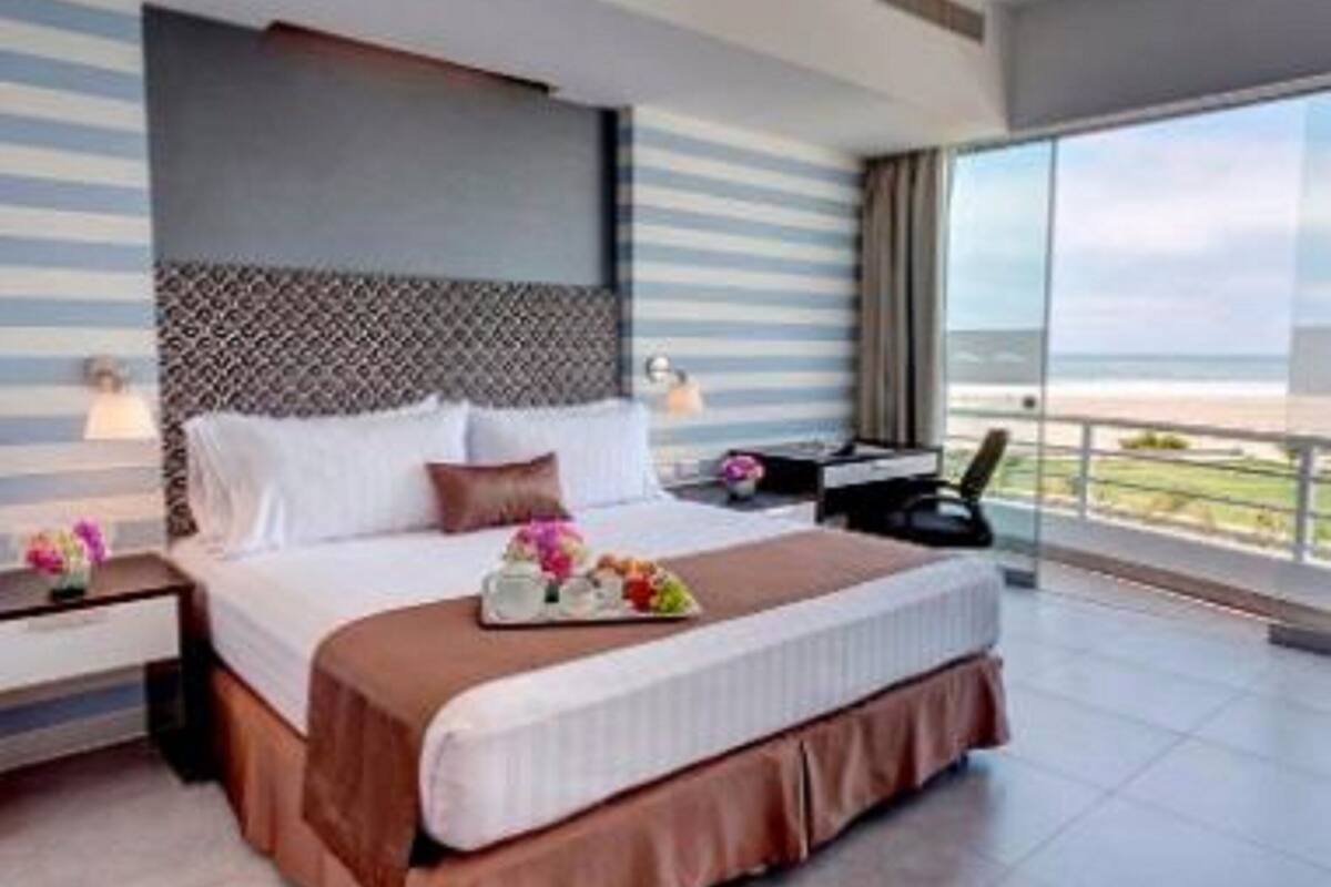 A modern hotel room with a large bed, a nightstand, a desk, and a view of the beach.