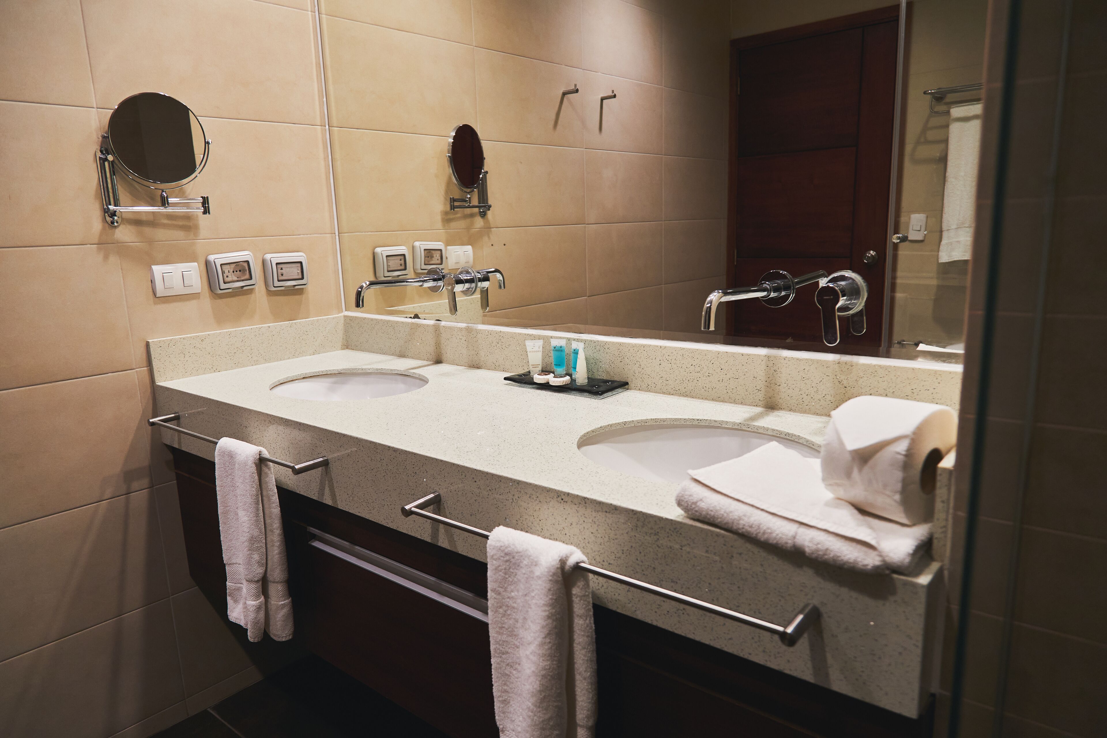 A modern bathroom with two sinks, a large mirror, and towel racks.