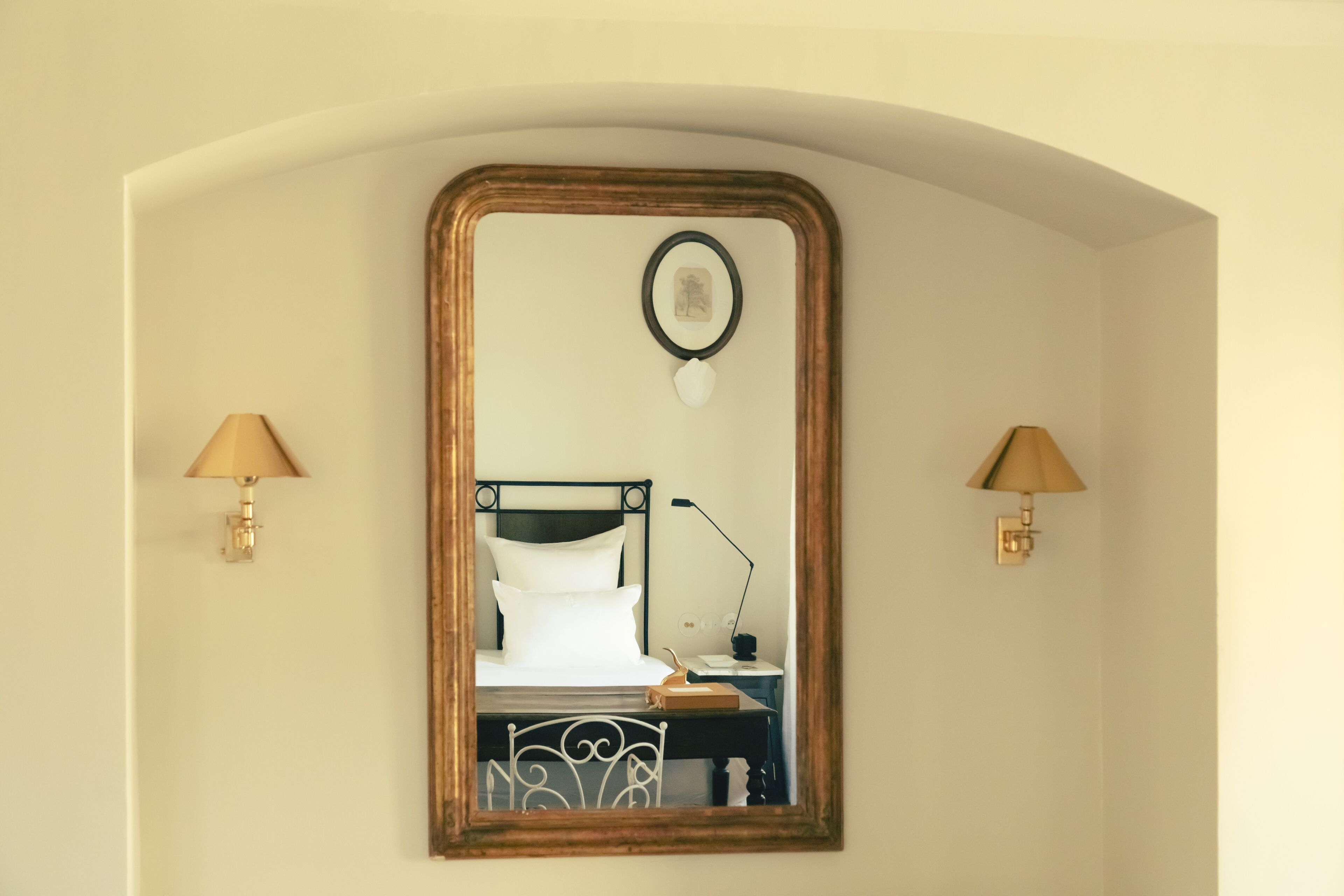 Un dormitorio con cama, mesita de noche, lámpara y un espejo con marco decorativo.