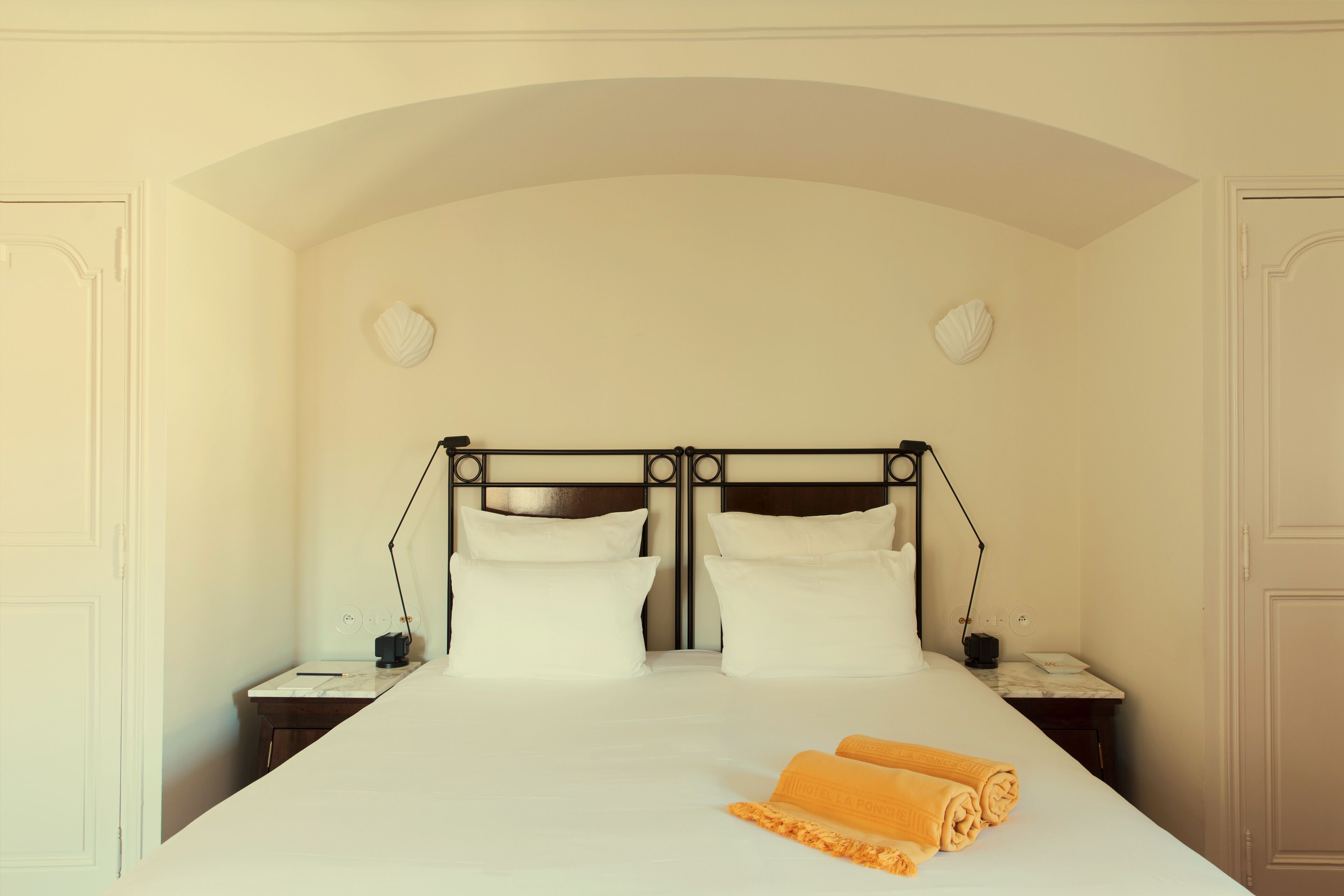 Habitación de hotel con una cama grande, dos mesitas de noche y un cabecero con un arco curvo.
