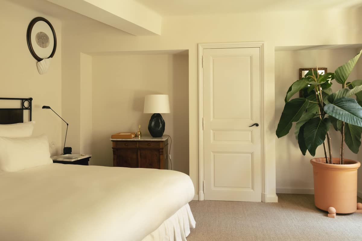 Un dormitorio con cama, mesita de noche, lámpara, cómoda y una planta en maceta.