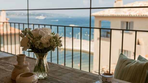 A balcony with a view of the sea, a vase of flowers, and a cup of coffee on a wooden table. - Hôtel La Ponche (Saint-Tropez)