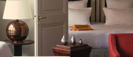 A hotel room with two beds, a sitting area with a chair, a lamp, and a small table with decorative items.