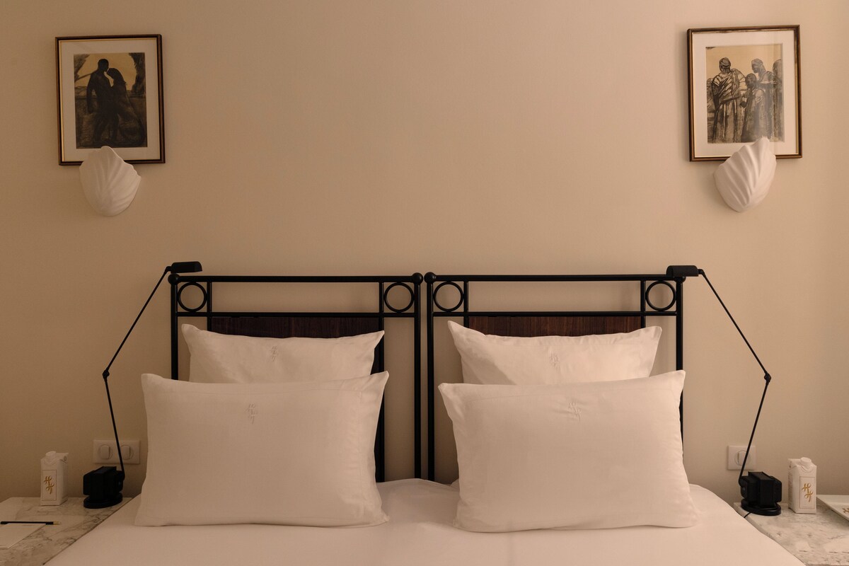 A bed with white pillows and a metal headboard, two bedside tables with lamps, and framed pictures on the wall.