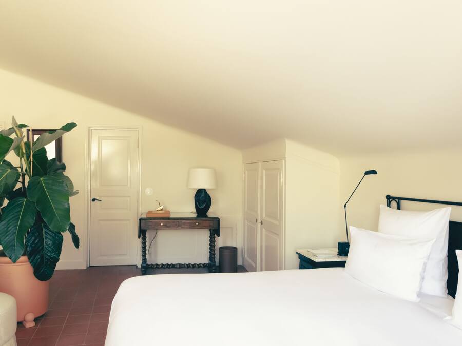 Una habitación de hotel con una cama, una mesita de noche, una lámpara, una planta en maceta y una puerta.