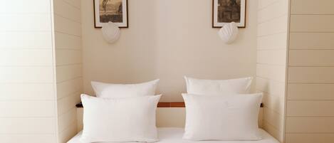 A neatly made bed with white linens and pillows, framed pictures on the wall, and a wooden headboard.