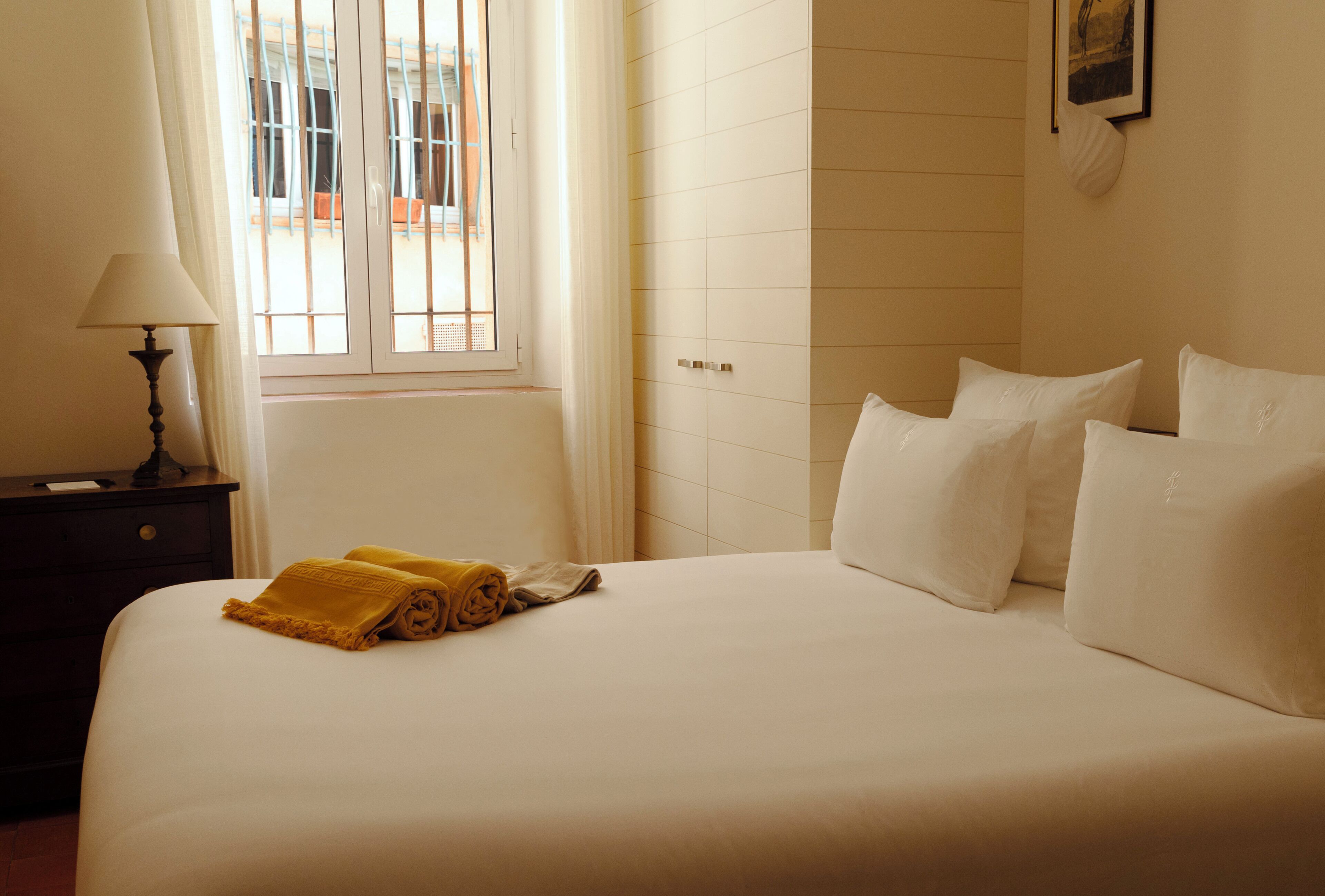 Una habitación de hotel con cama, mesita de noche, lámpara y ventana con cortinas.
