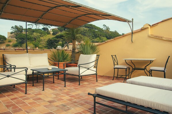 Una terraza con mobiliario exterior, incluyendo un sofá, sillas y una mesa, bajo un toldo.