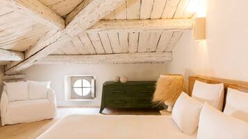 A bedroom with a sloped ceiling, a bed with white linens, a green dresser, and a small window.