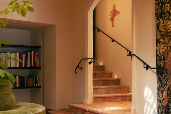 A staircase with a black handrail, a wall with a floral tapestry, and a bookshelf with books. - Hôtel La Ponche (Saint-Tropez)