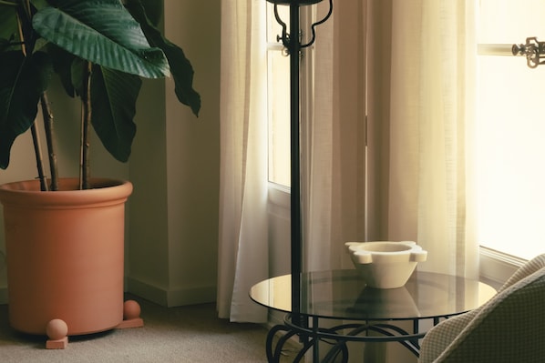 A corner of a room with a potted plant, a glass table with a bowl, and a window with curtains. - Hôtel La Ponche (Saint-Tropez)