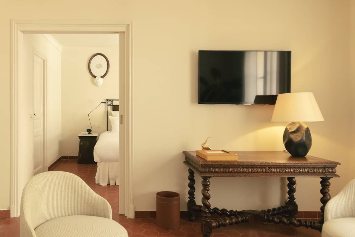 Una habitación de hotel con una cama, una mesita de noche con lámpara, un televisor en la pared y una silla.