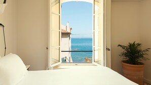 A room with a bed, a potted plant, and a window with a view of the sea and buildings. - Hôtel La Ponche (Saint-Tropez)