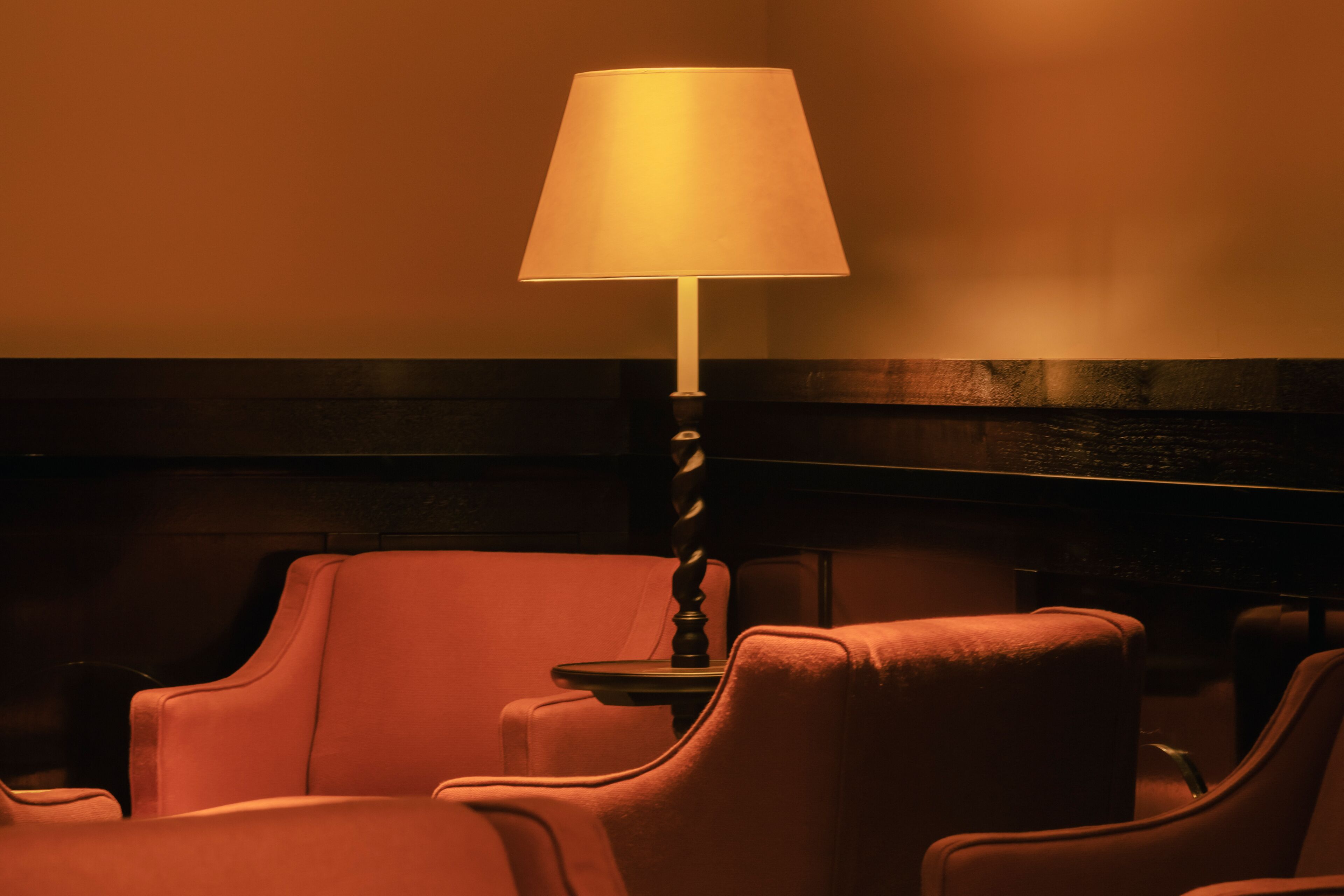 A room with a single table lamp, a wooden headboard, and two plush armchairs.