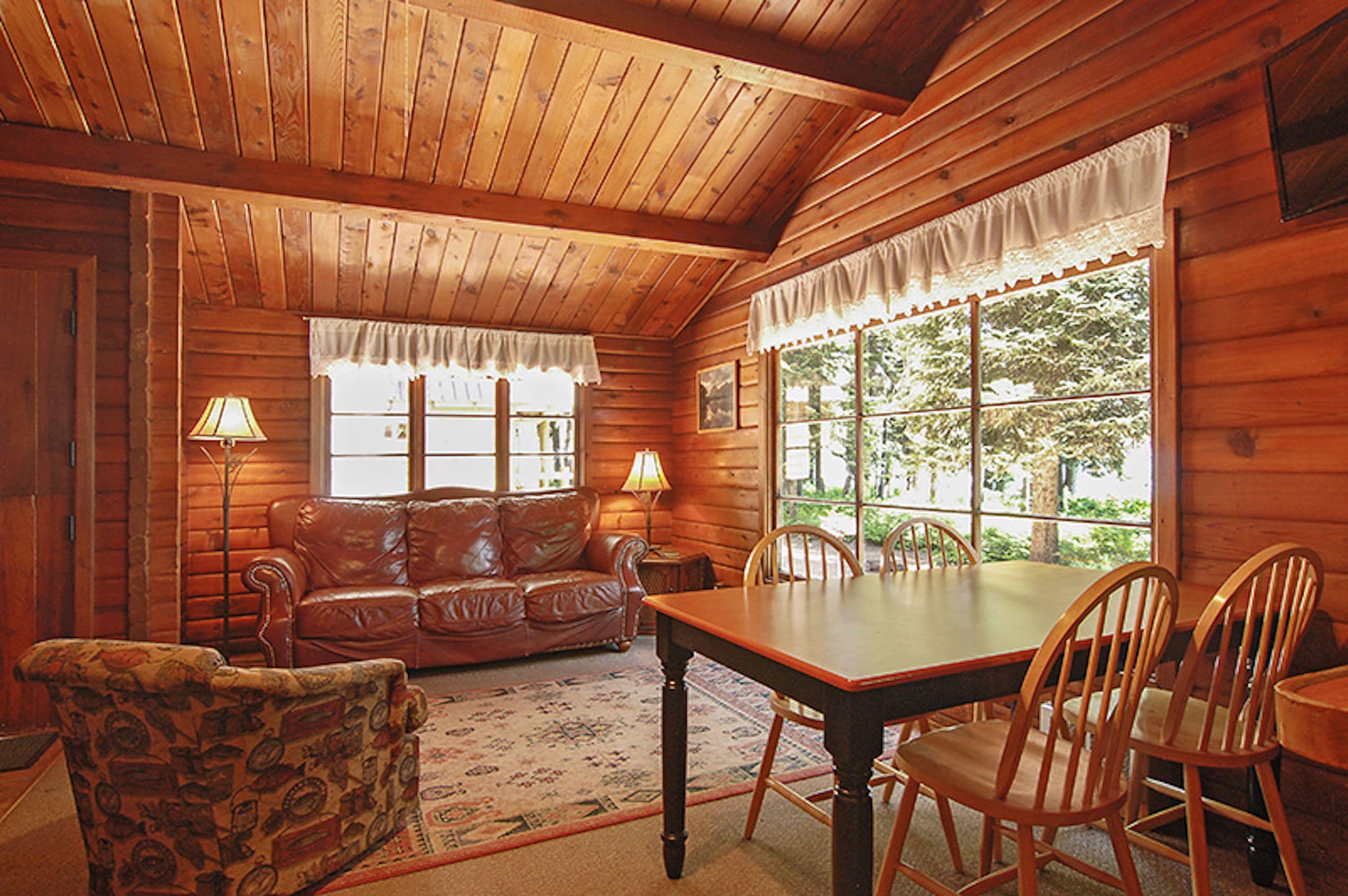 L’intérieur d’un chalet en bois, avec une table et des chaises en bois, un canapé en cuir et un fauteuil à motifs.