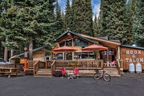 Une cabane rustique en rondins de bois, avec une épicerie, des sièges à l'extérieur et un panneau représentant un crochet et une griffe.