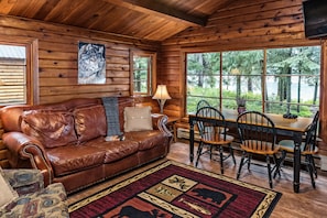 A cozy cabin interior with a leather couch, wooden dining table, and chairs. - Shelter Cove Resort and Marina (Crescent)