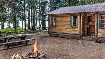 A rustic cabin with a fire pit, wooden deck, and a view of a forested lake.