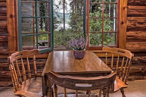 A wooden dining table with two chairs, a vase with flowers, and a view of a lake through open windows. - Shelter Cove Resort and Marina (Crescent)