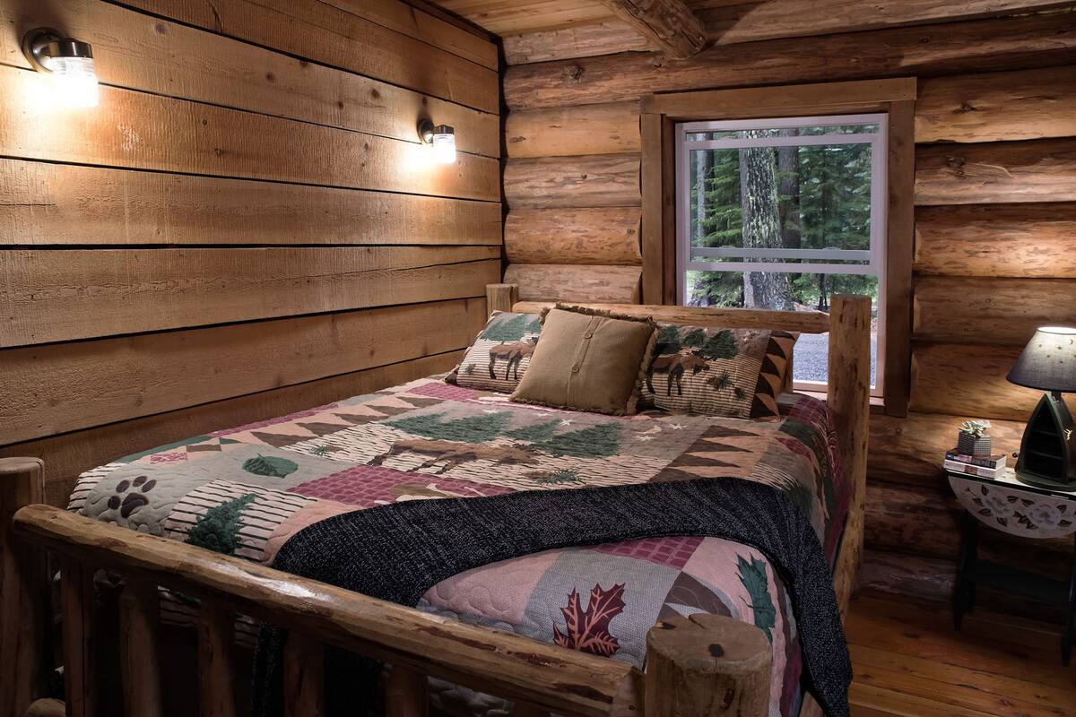 Een houten kamer met een bed, een raam en een lamp op een nachtkastje.