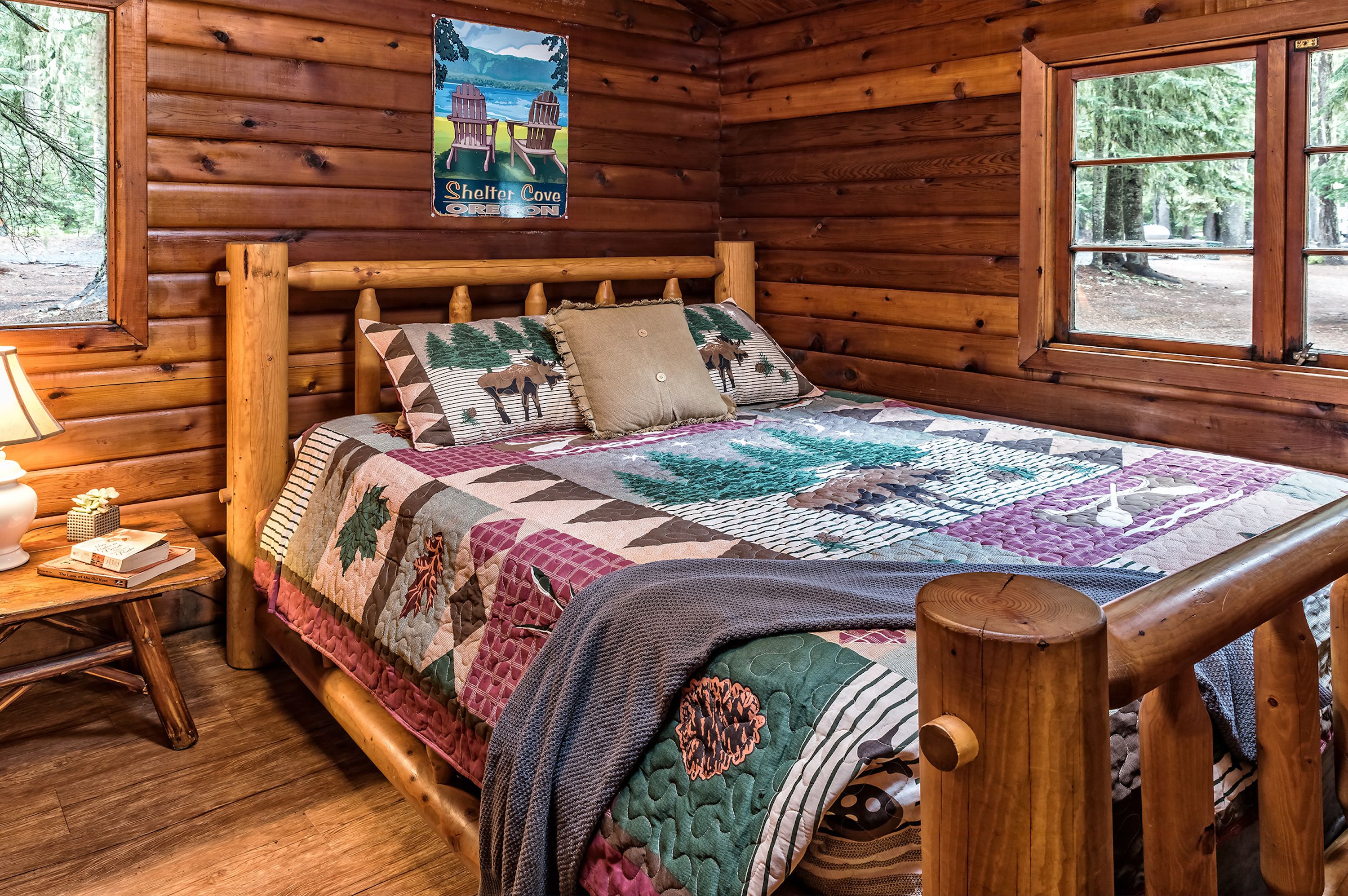 Une chambre dans une cabane en bois, avec un lit, une affiche, une fenêtre et une table de chevet.