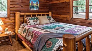 Une chambre dans une cabane en bois, avec un lit, une affiche, une fenêtre et une table de chevet.