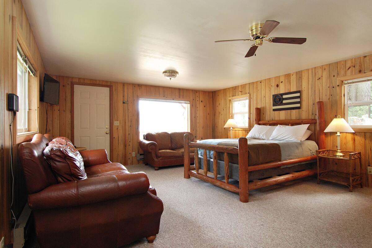 Een gezellige kamer met een houten bed, een leren bank, een nachtkastje van hout en een plafondventilator.