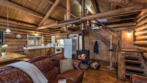 Interior de una cabaña de troncos con chimenea, escalera de madera y sofá de cuero.