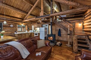 Interior de una cabaña de troncos con chimenea, escalera de madera y sofá de cuero.