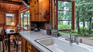 Cocina de cabaña de madera con un ventanal grande, un lavabo y un comedor con sillas y una mesa.