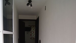 Un pasillo estrecho con pisos y paredes de baldosas blancas, que conduce a una habitación con una puerta.