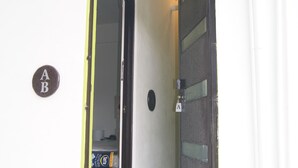 Un marco de puerta amarillo, una puerta con panel de vidrio y una pequeña señal con las letras "AB" en la pared.