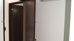 Una habitación con puerta cerrada, un equipo de aire acondicionado instalado en la pared y suelo de baldosas.