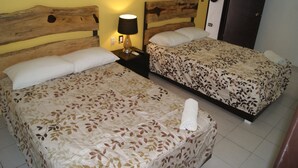 Habitación de hotel con dos camas, cada una con cubrecama floral, cabecero de madera, mesita de noche con lámpara y una toalla en el suelo.