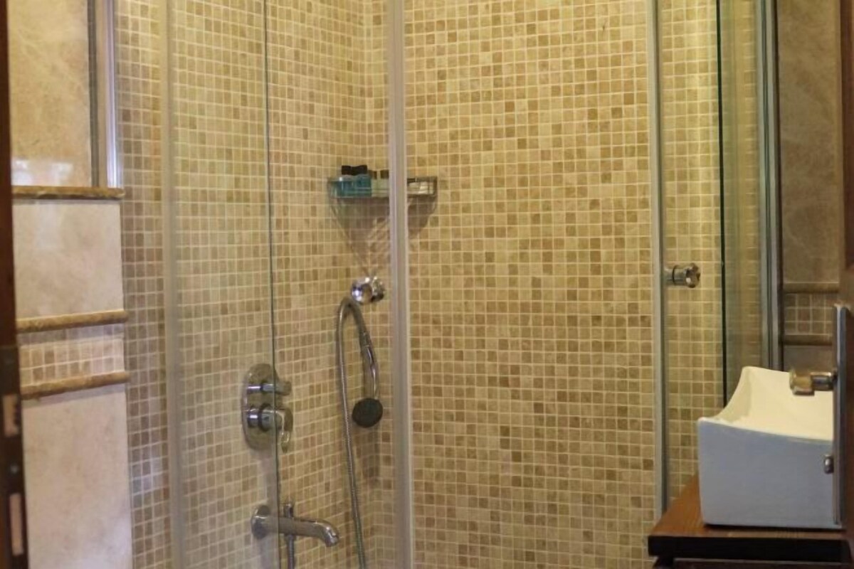 A shower with a glass door, tiled walls, and a white sink.