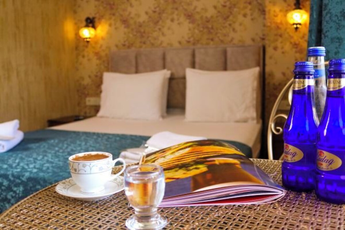 A hotel room with a bed, a table with a book, a cup of coffee, and bottles of water.