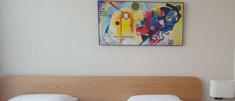 A hotel room with two beds, a wooden headboard, a nightstand with a lamp, and a colorful abstract painting on the wall.