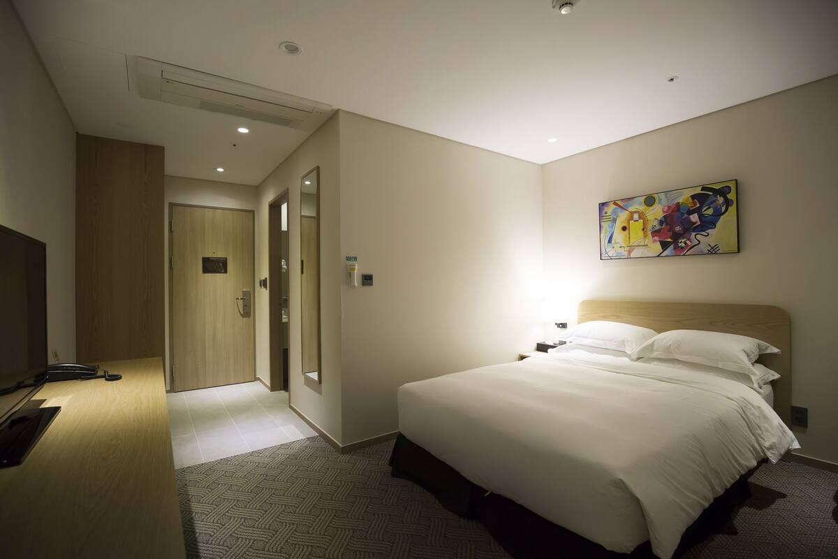 A hotel room with a bed, bedside table, and a painting on the wall.